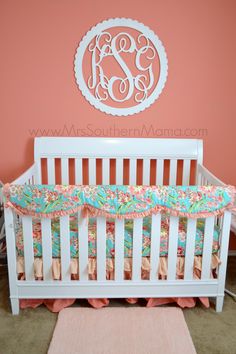 a white crib with pink and blue bedding in front of a monogrammed wall