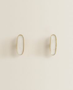 two small white and gold earrings sitting on top of each other in front of a white wall