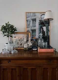 a wooden cabinet topped with bottles and glasses next to a framed photograph on the wall