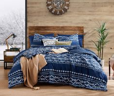 a bed with blue and white comforter next to a wooden wall