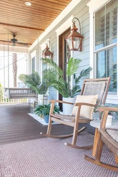 a porch with rocking chairs and potted plants on the front porch, along with hanging lanterns