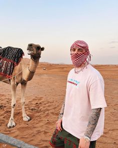 a man standing next to a camel on top of a sandy field with an instagram message