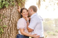 a man and woman hugging each other next to a tree