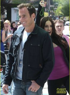 a man in black jacket standing next to a woman with her hand up and smiling at the camera