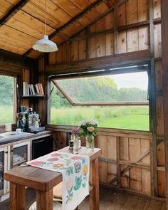 a table and chairs in a room with wood paneling on the walls, windows overlooking a field