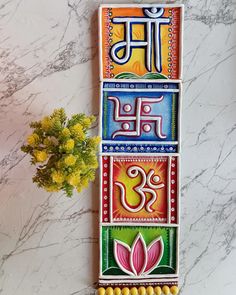 a colorful wall hanging on the side of a building with flowers in front of it