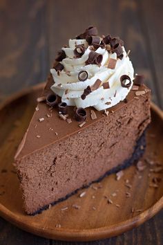 a piece of chocolate cake with whipped cream and chocolate chips on top, sitting on a wooden plate