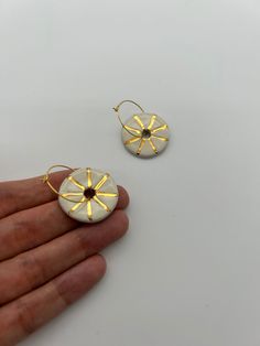 two small white and gold earrings in the shape of sunflowers on a hand