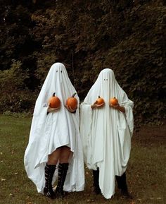 two people in white ghost costumes holding pumpkins