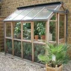 a small greenhouse with plants in it and brick wall behind the building that has windows on both sides