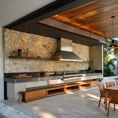 an outdoor kitchen and dining area with stone walls, wood ceilinging and wooden chairs