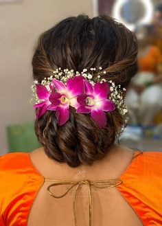 the back of a woman's head with flowers in her hair and an orange dress