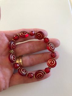 "Beautiful holiday red Czech glass spiral beads and ruby red shimmering Picasso glass with antique gold accents on a stretch bracelet. Matte red and gold puffy spiral coin beads are 12 x 14 mm with translucent Picasso glaze. Alternating 8 mm ruby red beads with gold Picasso finish. Lovely beads are accented with antique gold plated daisies and beaded spacers by Tierracast made in USA. Made to order in your size. Bracelet is made on professional stretch elastic. Example is about 7\" and fits a 6\ Red Stretch Bracelet With Round Beads For Gift, Red Stretch Bracelet With Round Beads For Gifting, Red Spiritual Stretch Bracelet With Round Beads, Spiritual Red Round Beads Stretch Bracelet, Holiday Red Adjustable Jewelry, Red Beaded Stretch Bracelet Gift, Red Beaded Stretch Bracelet As Gift, Red Bracelet Jewelry For Holidays, Spiritual Red Stretch Bracelet Gift