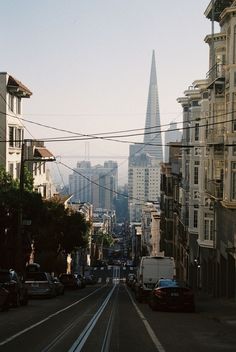 a city street with cars parked on both sides and tall buildings in the back ground