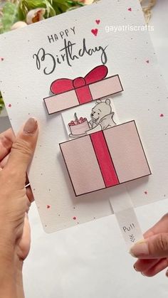 someone holding up a card with a teddy bear in a gift box on top of it