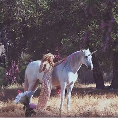 a woman standing next to a white horse on top of a dry grass covered field