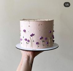 a hand holding a pink cake with purple flowers on it