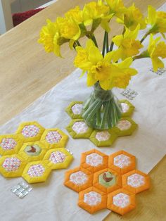 yellow flowers are in a vase next to small hexagons on a table