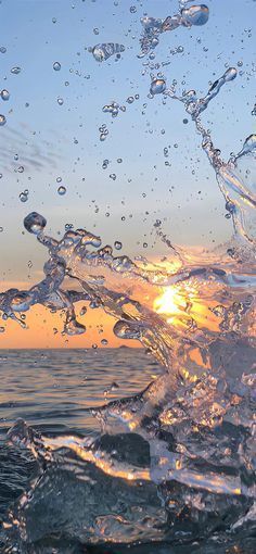 water splashing on the rocks in front of an orange sun setting over the ocean