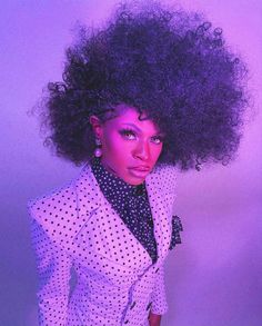 a woman with an afro wearing a polka dot suit and black tie, standing in front of a purple background