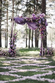 an outdoor ceremony with purple flowers and greenery on the ground, surrounded by trees