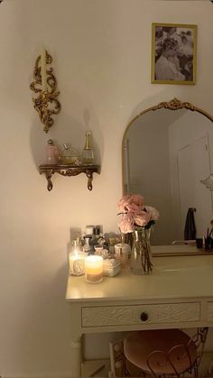 a vanity with flowers and candles on it in front of a mirror, wall hangings