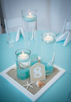 there are three candles in the center of this table with sand and starfish around it