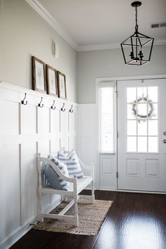 a white bench sitting in the middle of a room next to a door with hooks on it