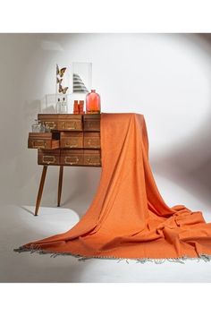 an orange blanket draped over a dresser with a vase and candle on the end table