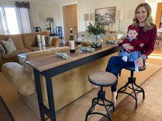 a woman holding a baby sitting on top of a stool next to a kitchen island