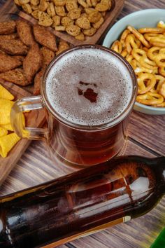 a beer in a mug next to some snacks on a wooden table with a bottle of beer