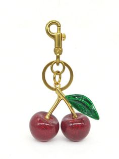 two cherries are attached to a gold keychain with a green leaf on it