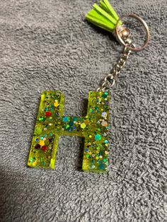 the letter h is made out of glitter and has a tassell on it