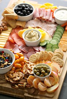 an assortment of snacks and dips on a cutting board with cheese, crackers, olives