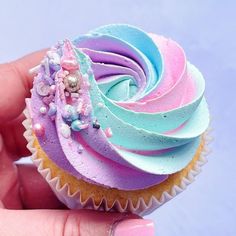 a hand holding a cupcake with pastel frosting and sprinkles