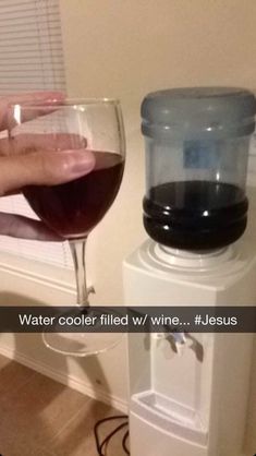 a glass of wine sitting on top of a water cooler next to a person's hand