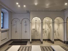 a bathroom with white tile and black and white checkerboard flooring, three urinals on either side of the shower