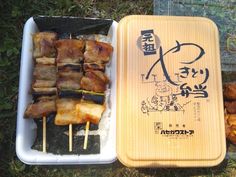 there are many different foods in the trays on the grass, including meat and vegetable skewers