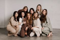 a group of women sitting next to each other posing for a photo in front of a white wall