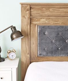 a bed with a wooden headboard next to an alarm clock on a night stand