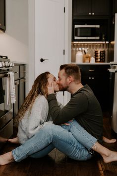 a man and woman sitting on the floor in front of an oven kissing each other