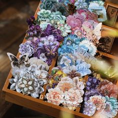 there are many small flowers in the box on the wooden table and one is purple