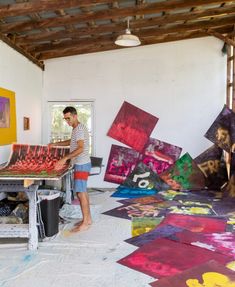 a man standing in a room with paintings on the floor and walls, while another person is painting