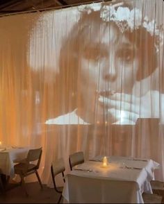 an image of a woman's face is projected on the wall behind two tables