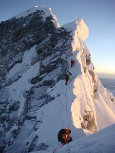 several people climbing up the side of a snow covered mountain