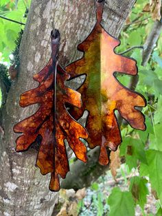 two metal leaves hanging from a tree in the woods, one is brown and orange