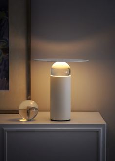 a white table lamp sitting on top of a wooden shelf next to a glass bowl