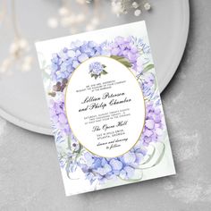 a wedding card with purple flowers and greenery on the front is displayed next to a plate