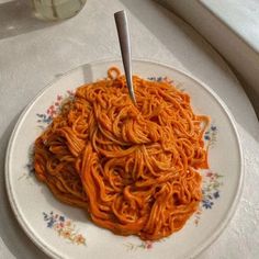 a white plate topped with pasta and sauce on top of a table next to a window