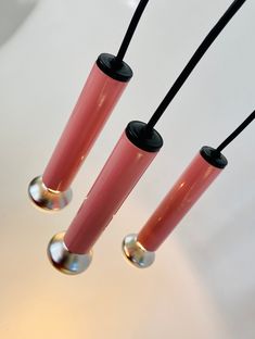 three pink vases with black handles are hanging from the ceiling